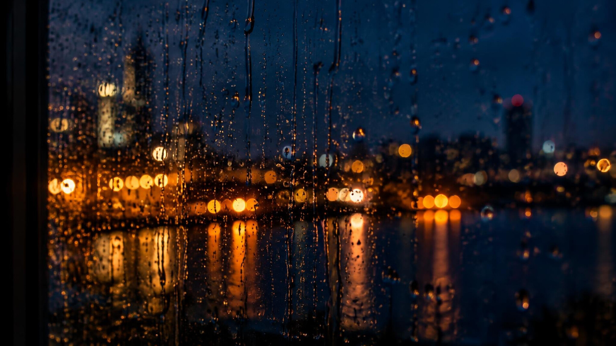 Raindrops on a dark window with blurred city lights beyond